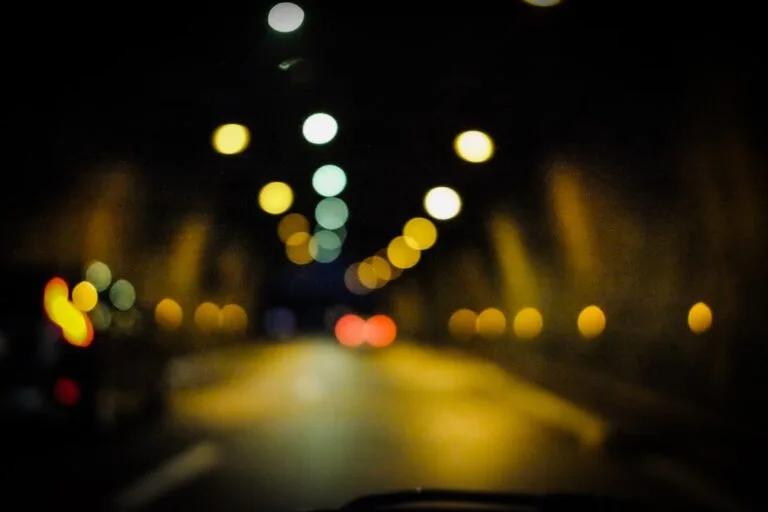 Vue floue de la route la nuit depuis un véhicule, halos colorés autour des lumières