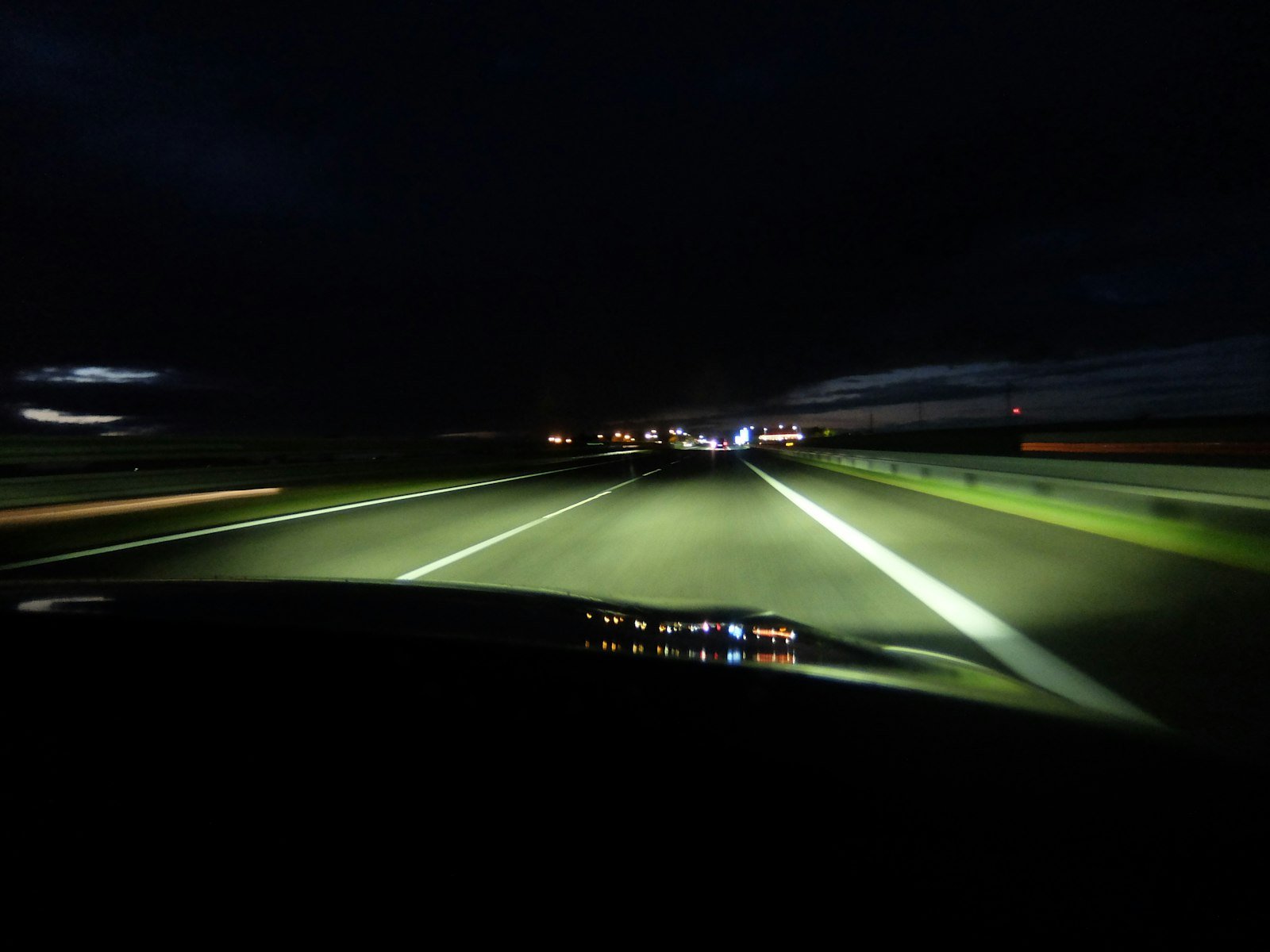 View from inside a car driving at night on a motorway, headlights and distant lights