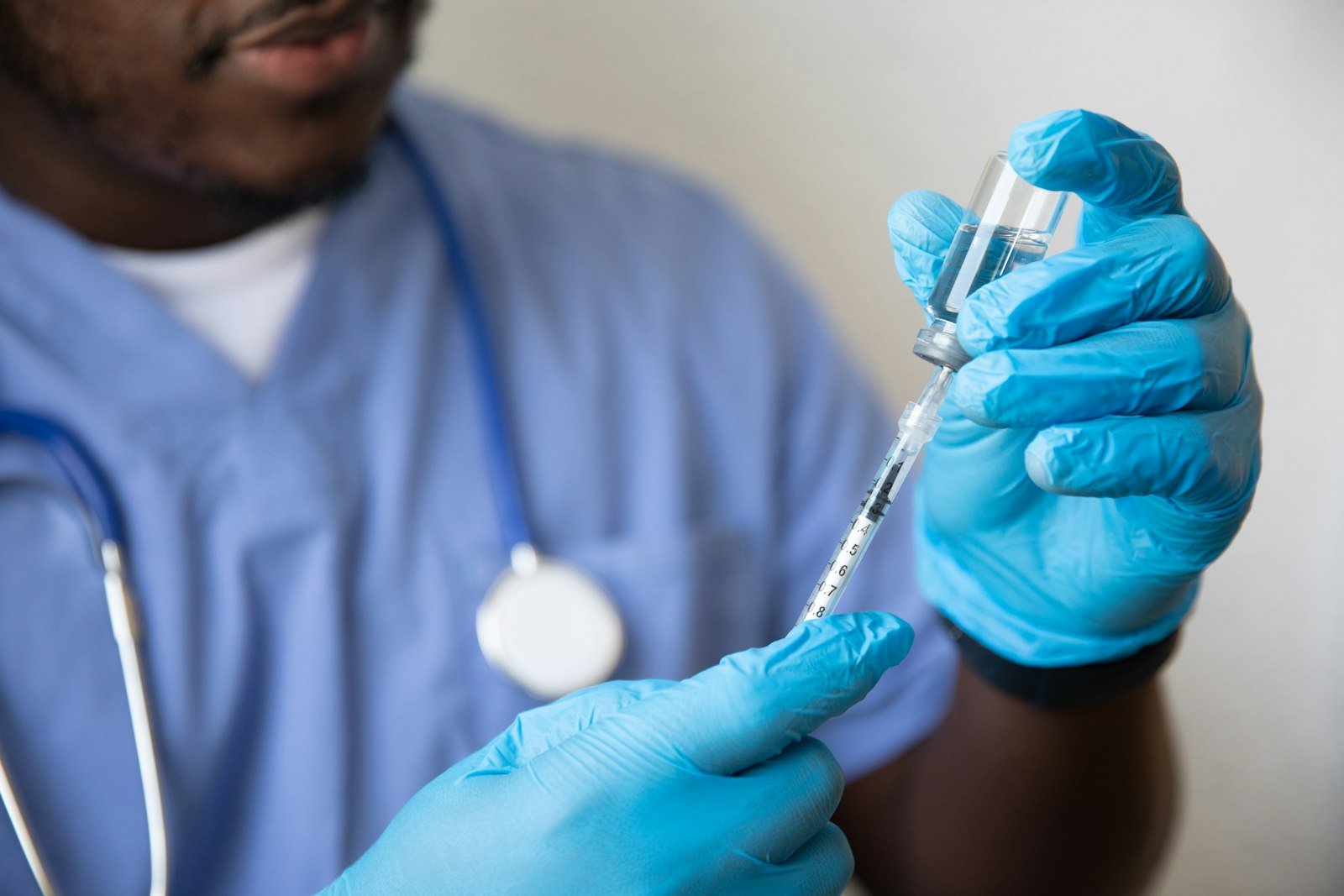 Mains gantées prélevant une dose dans un flacon à l'aide d'une seringue graduée
