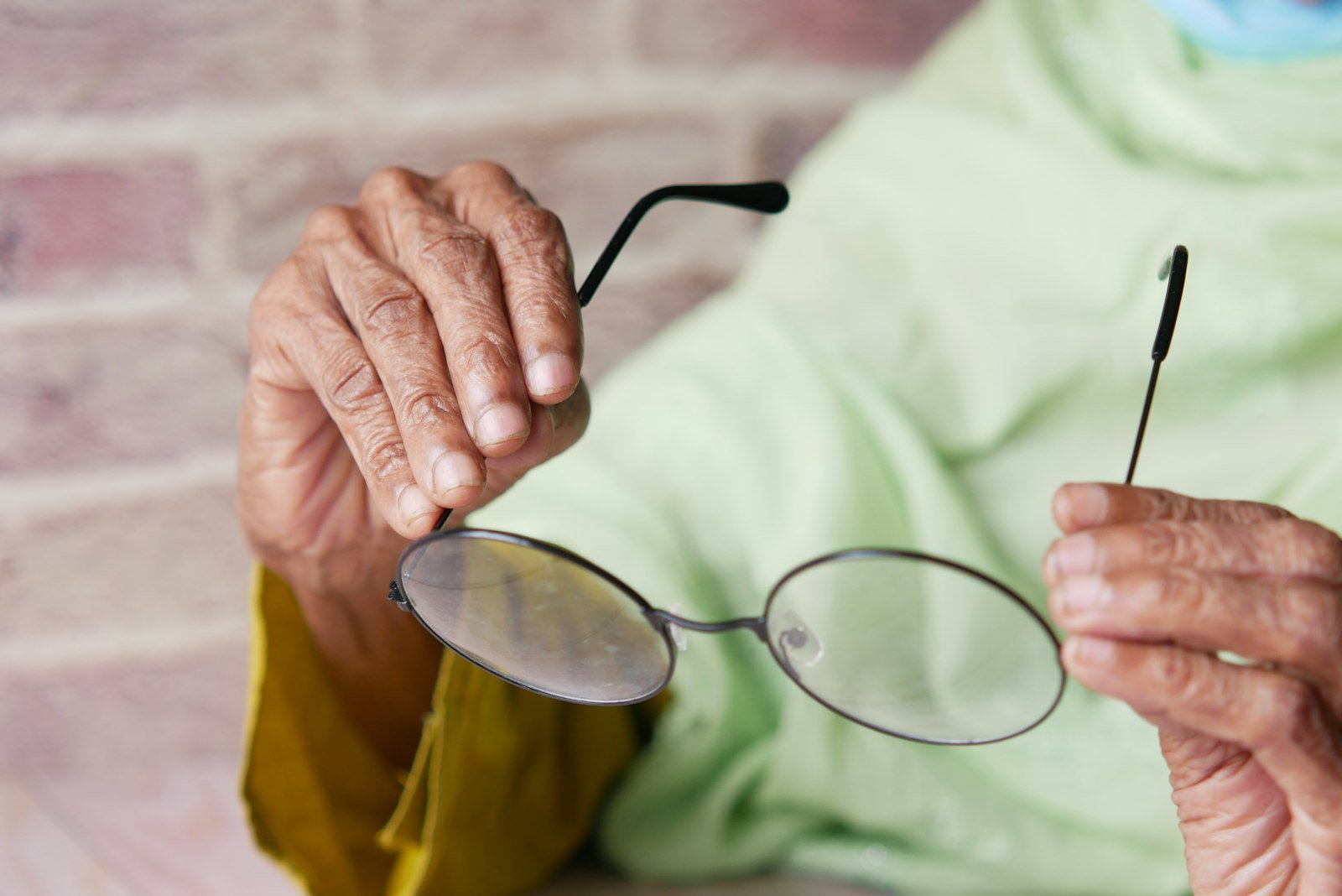 Hands of an elderly woman holding a pair of round glasses