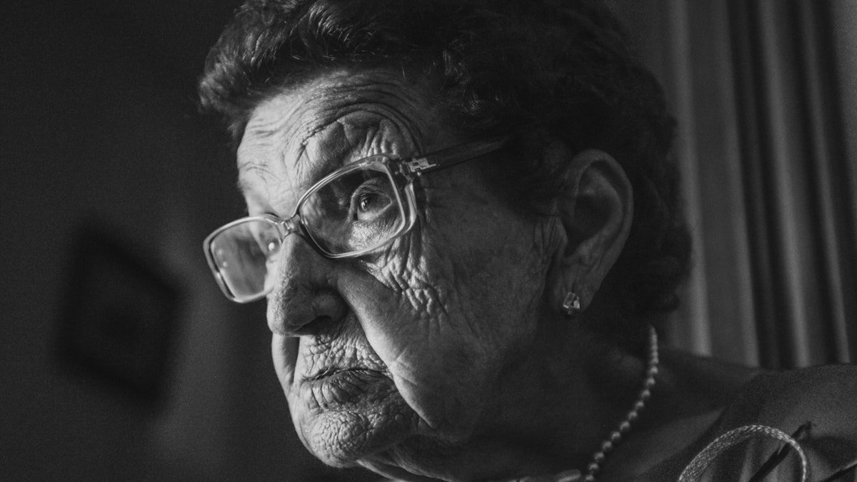 Portrait en noir et blanc d'une femme âgée portant des lunettes, regard tourné vers la lumière