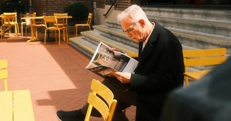 Homme âgé lisant un journal, lunettes sur le nez, assis en terrasse