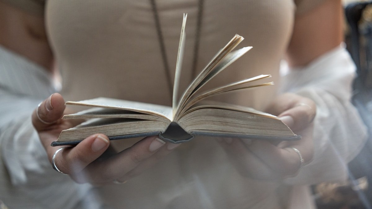 Deux mains tenant un livre ouvert, pages tournées vers le lecteur