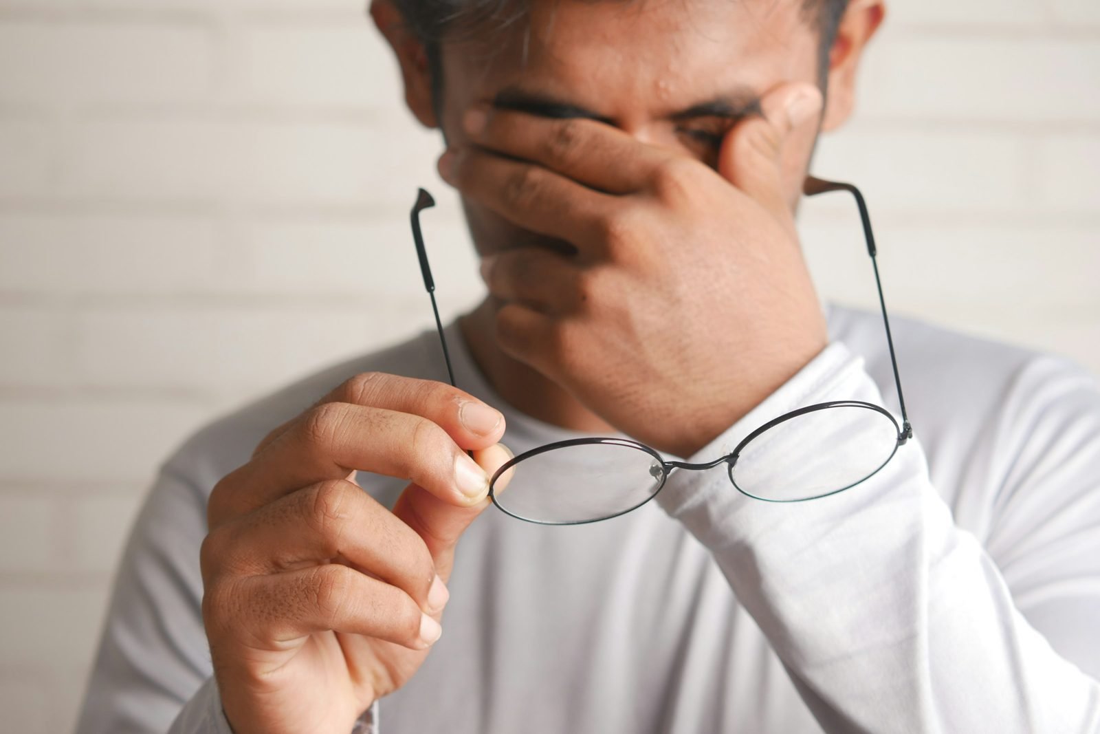 Homme retirant ses lunettes et se pinçant la racine du nez, signe de fatigue visuelle