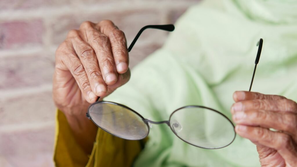 An elderly female patient is holding a pair of glasses in her hand
