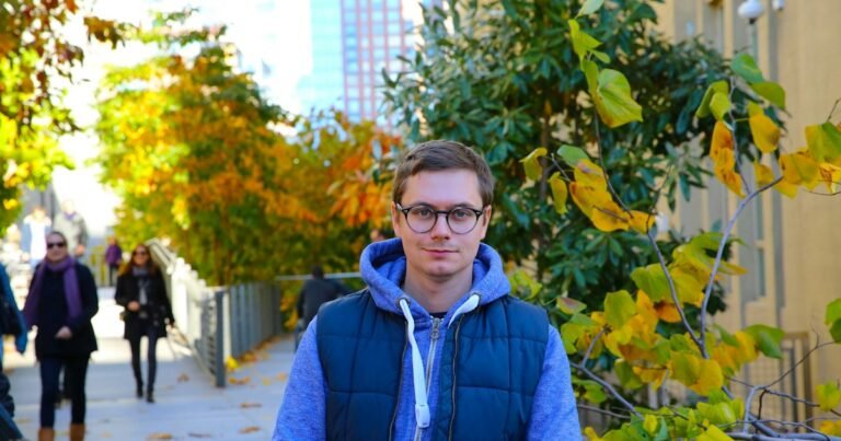 Young man wearing glasses on a tree-lined street in autumn