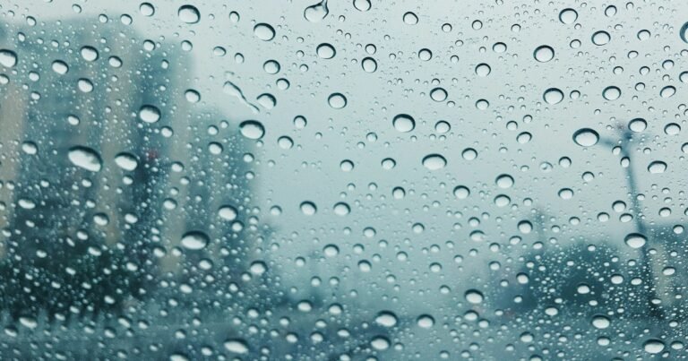Raindrops on a window, with a blurred landscape behind