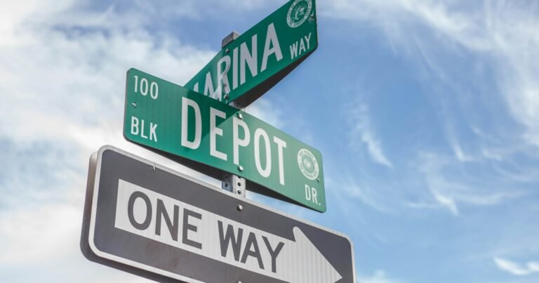 Street name signs and a one-way sign against a blue sky