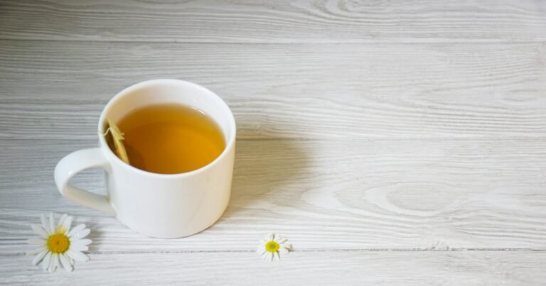 Cup of herbal tea on a white table with chamomile flowers