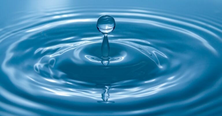 Water drop falling onto a blue surface and forming ripples